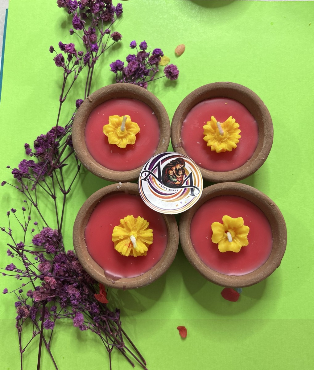 Four red clay diya candles with yellow wax flowers