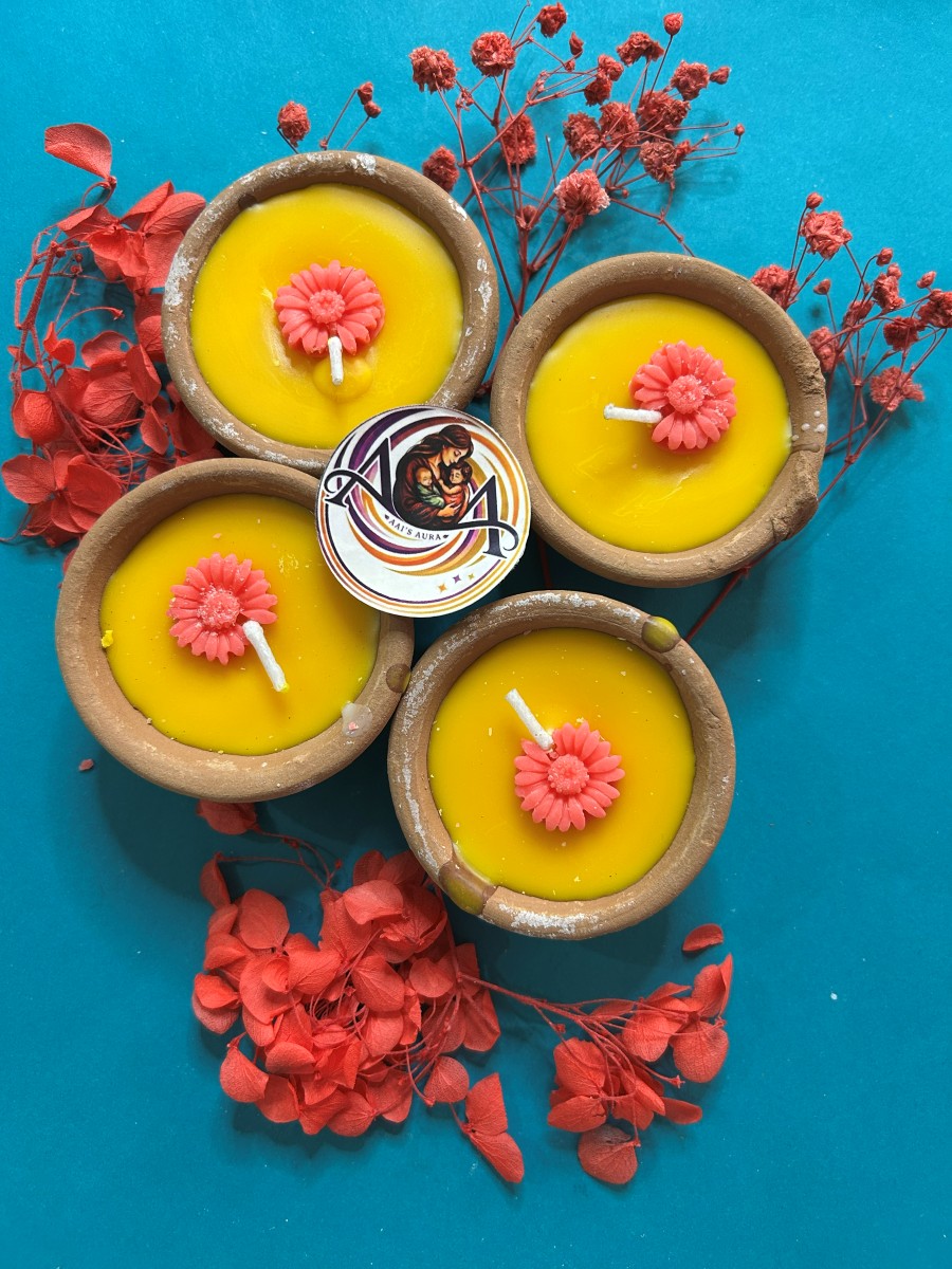 Four yellow clay diya candles with pink wax flowers