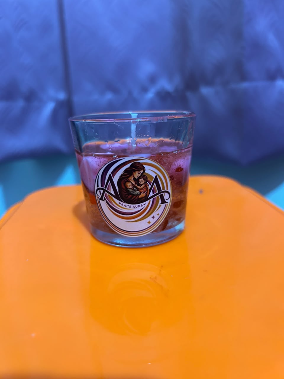 A clear glass with purple and amber wax on an orange surface