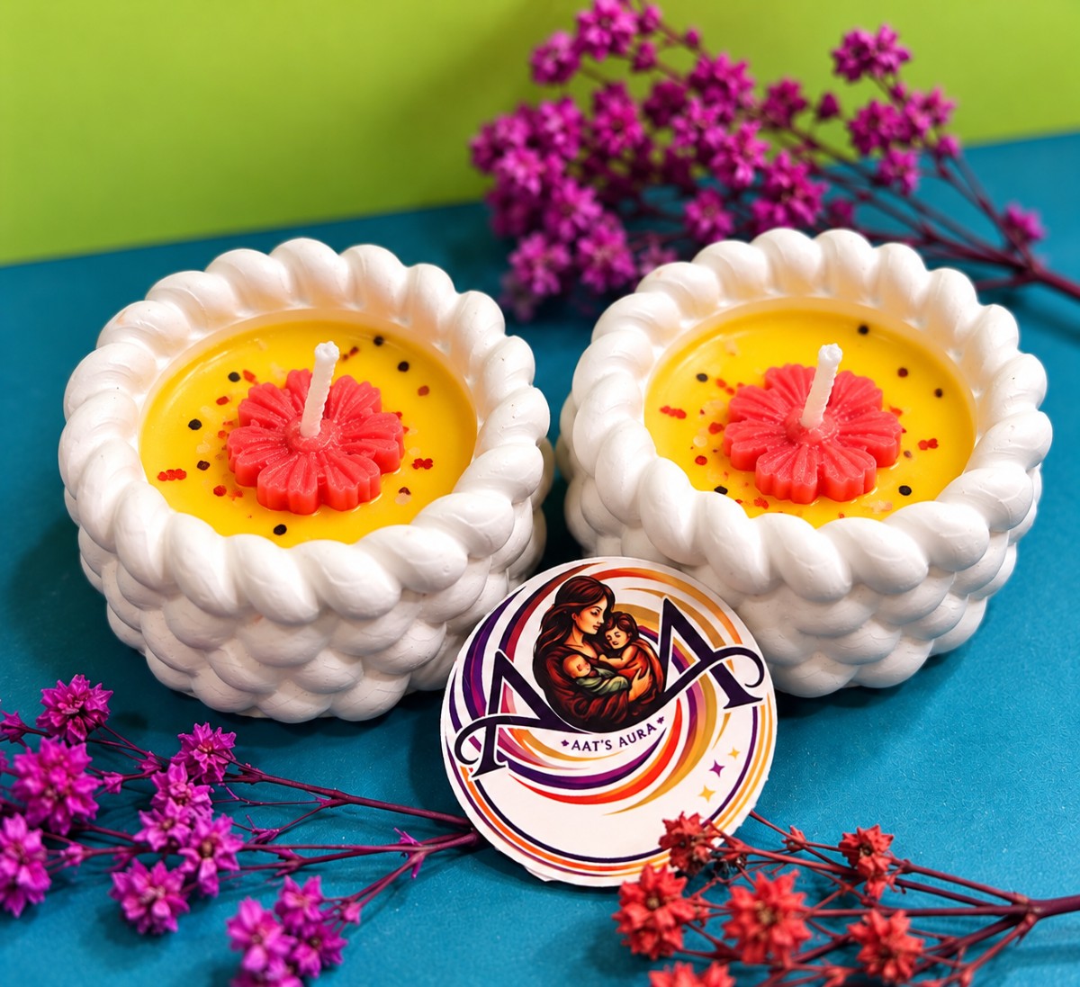 Two yellow marble diya candles with pink wax flowers