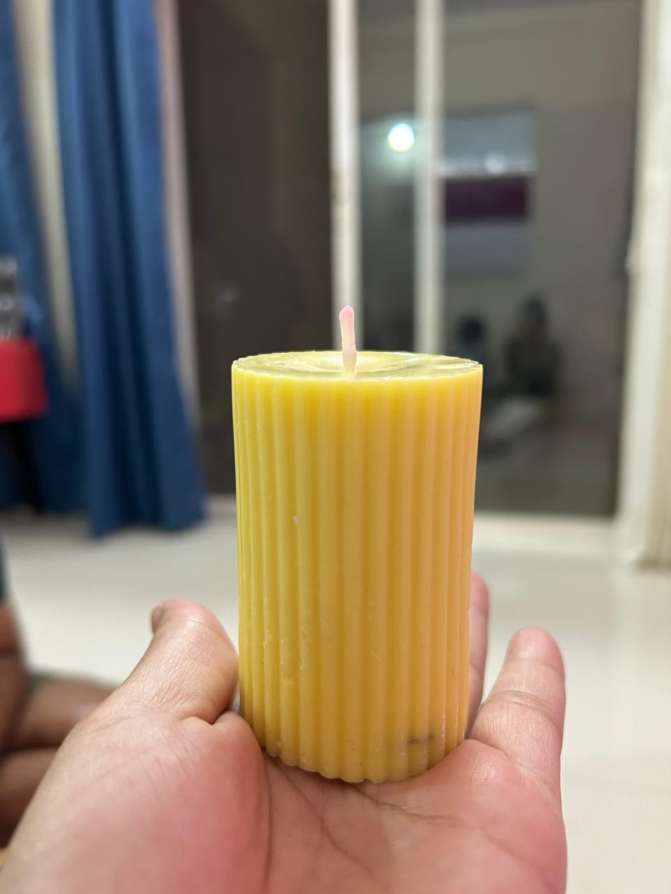 A yellow ribbed pillar candle held in a hand